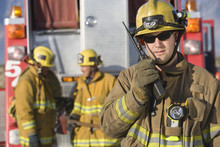 Portrait Of A Middle Aged Firefighter Talking On Radio With Colleagues Standing In The Background