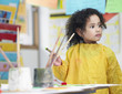 Cute little girl holding paintbrush in art class