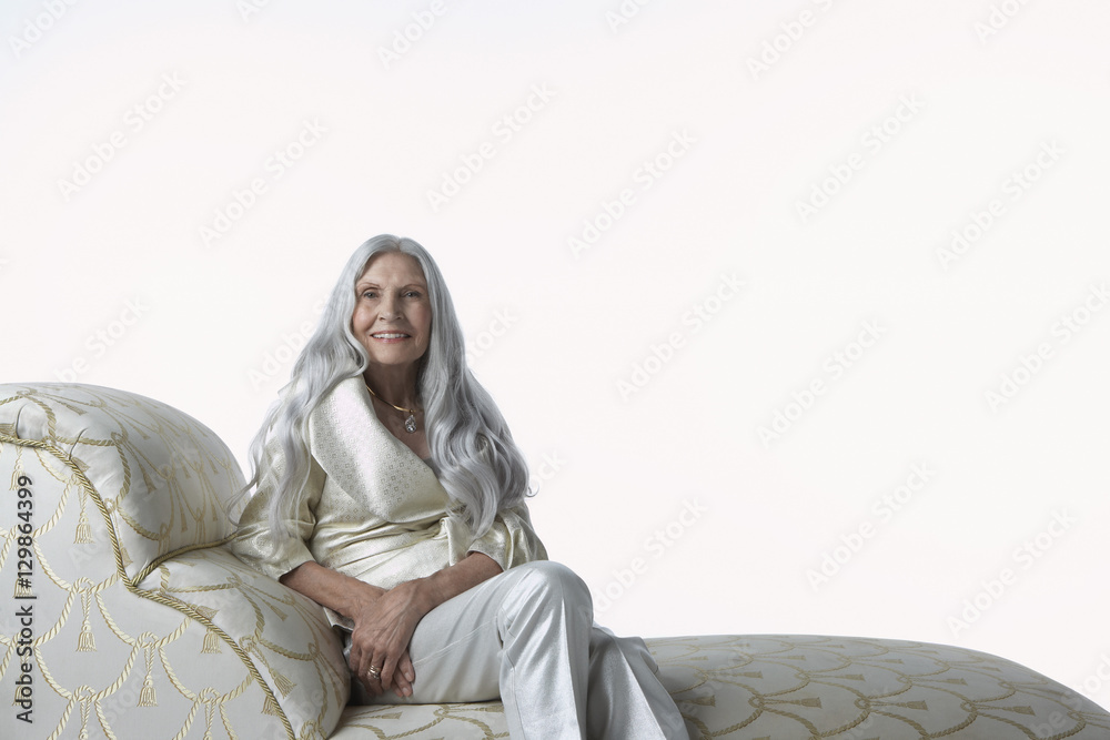 Portrait of an elegant senior woman sitting on chaise lounge against ...