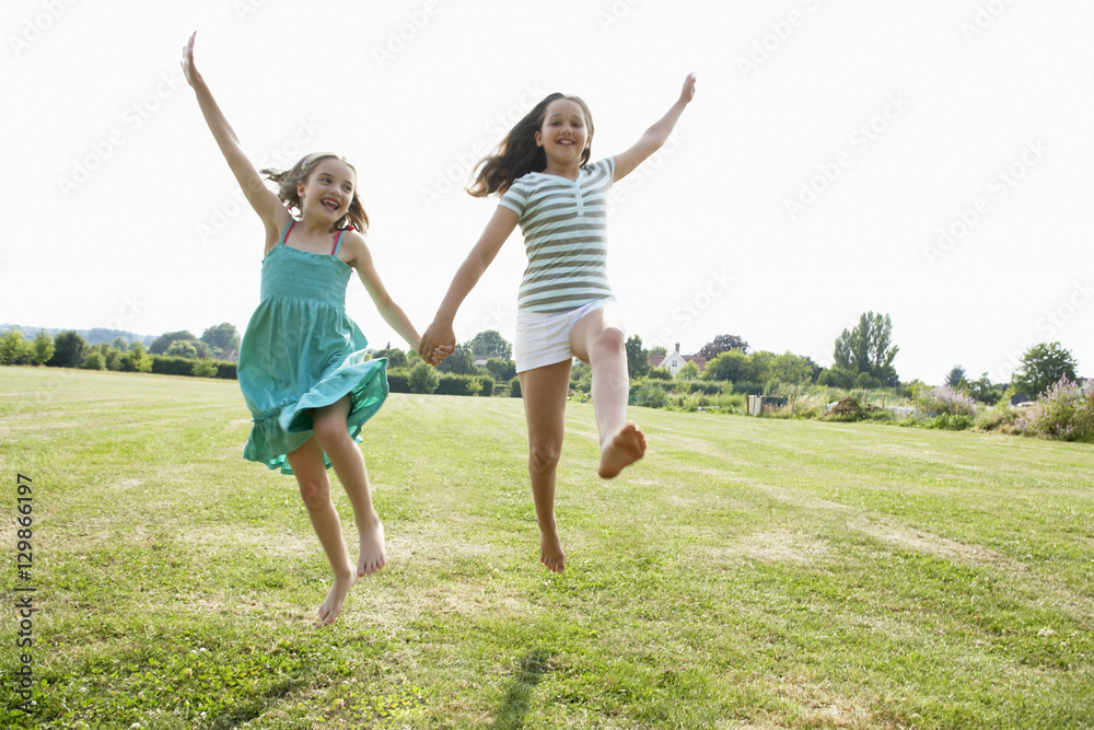 Two girls running and jumping hand in hand through field Stock Photo ...