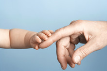 Closeup Of A Baby Holding Man's Finger Against Blue Background