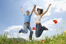 Low Angle Portrait Of Young Multiethnic Couple Jumping In Poppy Field Against Sky