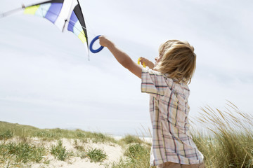 Side view of preadolescent boy flying kite on a windy beach