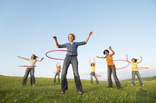 Full Length Of Happy Female Friends Playing With Hula Hoop Against Sky In Park