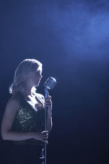 Side view of a young woman singing at microphone in smoky place