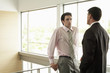 © moodboard - Young businessman looking at male colleague while standing by railing in office