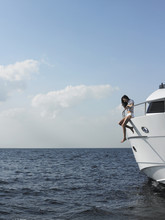 Side View Of Young Woman Sitting At Edge Of Yacht With Legs Dangling Overboard