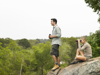 Wall Mural - Full length side view of a young man and woman on rock with binoculars looking at view