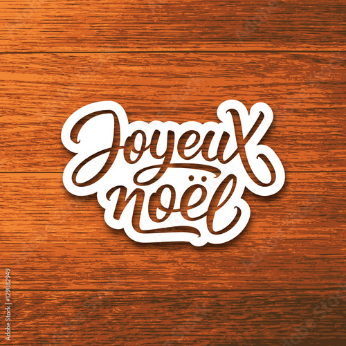 Joyeux Noel text on paper label with hand lettering over wood