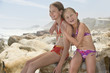 © MDBPIXS - Portrait of happy little girl sitting with sister on rocks at beach