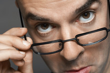 Closeup Portrait Of A Businessman With Hand On Glasses Making A Face Against Gray Background