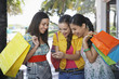 © MDBPIXS - Cheerful teenage girls with shopping bags text messaging outdoors