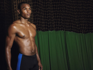 Shirtless confident young athlete standing against dark background