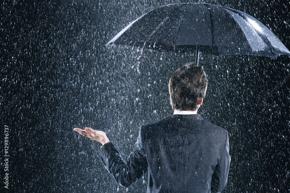 Rear view of a businessman staying dry under umbrella during downpour - obrazy, fototapety, plakaty 