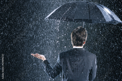 Fotomural Rear view of a businessman staying dry under umbrella during downpour