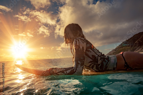 Zdjęcie XXL Surfingowiec dziewczyny dopatrywania zmierzch na surboard unosi się w błękitnym oceanie blisko skalistego brzeg