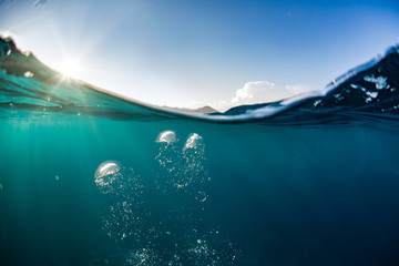 Wall Mural - ocean water line splits sky and underwaer part. air bubbles in deep blue. bright sun light and blue 