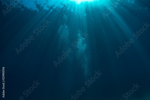 Fotomural Air bubbles underwater in deep blue ocean with sunrays and water surface