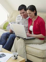 Wall Mural - Smiling young couple sitting at sofa with laptop and bills