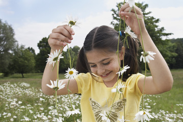 Wall Mural - Smiling young girl holding daisy chains in meadow