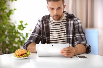 Sticker - Young man having snack while working with tablet computer in kitchen