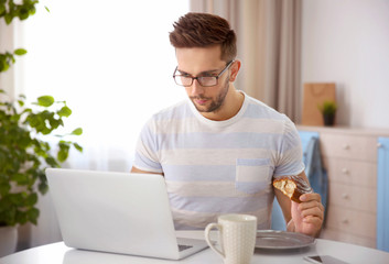 Sticker - Young man having snack while working with laptop in kitchen