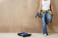 Lowsection Of A Young Woman With Toolbelt And Drill Leaning Against Wall