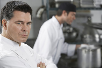 Wall Mural - Closeup of a serious chef with blurred colleague in the background in kitchen