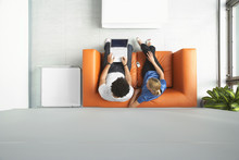 Full length top view of a man and woman using laptop on orange sofa in reception room at office
