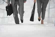Lowsection Of Two Businesspeople Walking Up Stairs With Bags In Office
