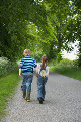 Full length rear view of a little boy and girl walking on country lane