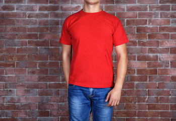 Sticker - Handsome young man in blank red t-shirt standing against brick wall, close up