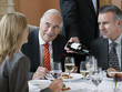 © MDBPIXS - Three businesspeople talking at restaurant table as waiter serves wine