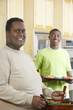 Portrait of an obese African American man preparing salad in kitchen with boy standing in background