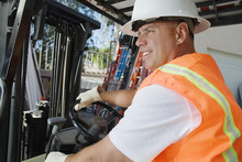 Happy Male Industrial Worker Driving Forklift At Workplace