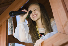 Happy Young Girl Dressed As A Pirate Looking Through Telescope From Window Of Playhouse