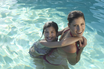 Wall Mural - Portrait of a happy mother giving daughter piggy back in swimming pool