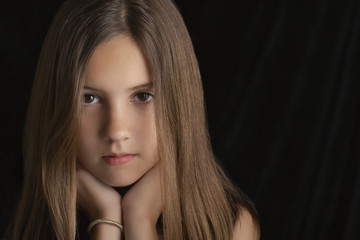 Closeup portrait of young brunette girl resting chin on hands against black background