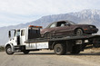 Damaged car being transported on tow truck with mountain range in the background
