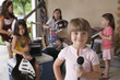 © moodboard - Portrait of cute young girl holding microphone with friends playing musical instrument in garage