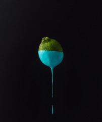 Wall Mural - lime with dripping blue paint on dark background. minimal food c
