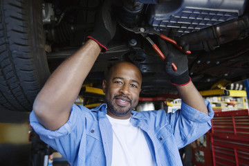 Portrait of a happy African American male mechanic beneath a car in garage