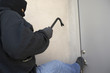 Burglar with crowbar kicking the door of house