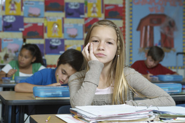 Portrait of a young girl getting bored while classmates writing notes in the background