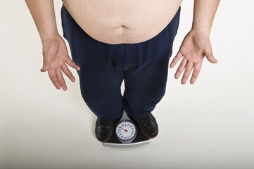 Low section of a young man measuring his weight on weighing machine