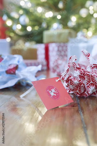 Fotografia, Obraz Unwrapped gift paper and tag on hardwood floor with Christmas tree in background
