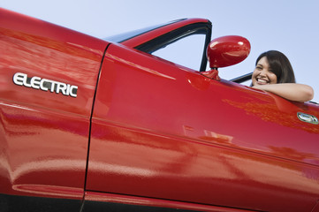 Side view portrait of a smiling woman in a red electric car