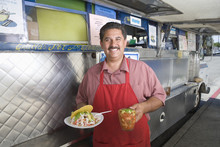 Portrait Of Happy Man Holding Snack And Refreshment Outside A Mobile Cafe Van