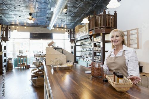 Cuadros en Lienzo Happy senior female spice merchant standing at counter while looking away in sto
