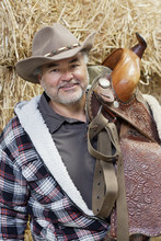 Portrait Of A Happy Mature Cowboy Carrying Saddle